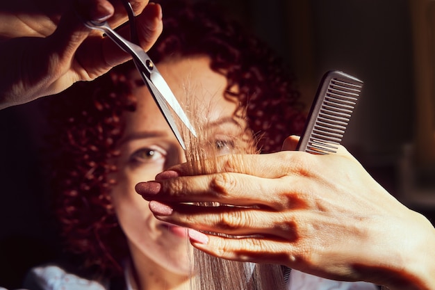 Imagem recortada de cabeleireiro aparando pontas de cabelo loiro