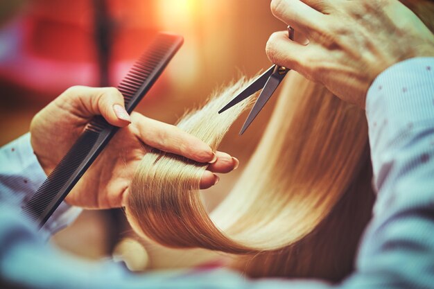 Imagem recortada de cabeleireiro aparando pontas de cabelo loiro