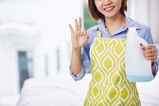 Imagem recortada de dona de casa sorridente com avental mostrando sinal de ok e frasco de sabonete líquido