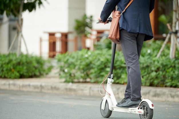 Imagem recortada de empresário ou estudante andando para trabalhar na scooter elétrica