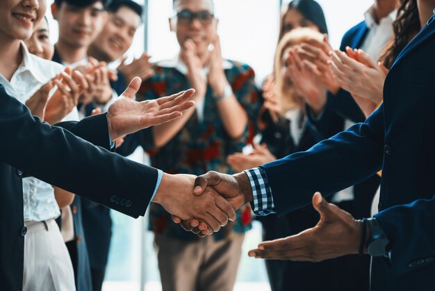 Imagem recortada de empresários apertando a mão e fazendo um contrato em sinal de cooperação de acordo arredondado com funcionários sorridentes aplaudindo e aplaudindo atrás Vista frontal Intelectual