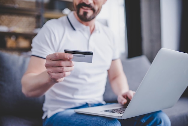 Imagem recortada de homem fazendo compras online com cartão de crédito e usando laptop em casa