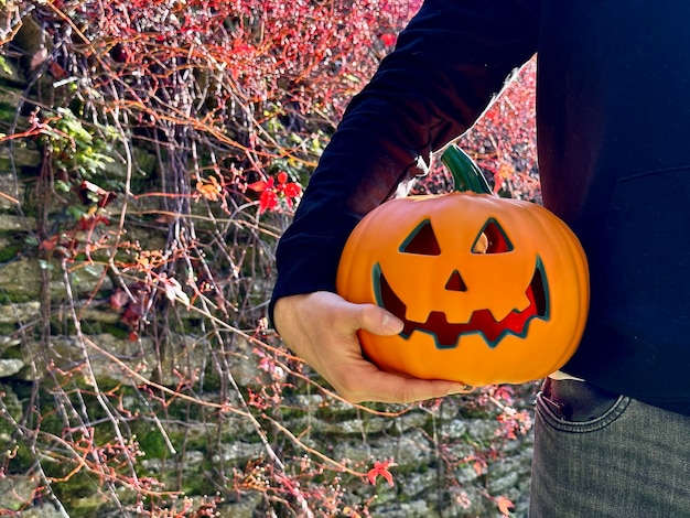 Foto imagem recortada de homem irreconhecível segurando folhas de outono vermelhas de abóbora de halloween no fundo