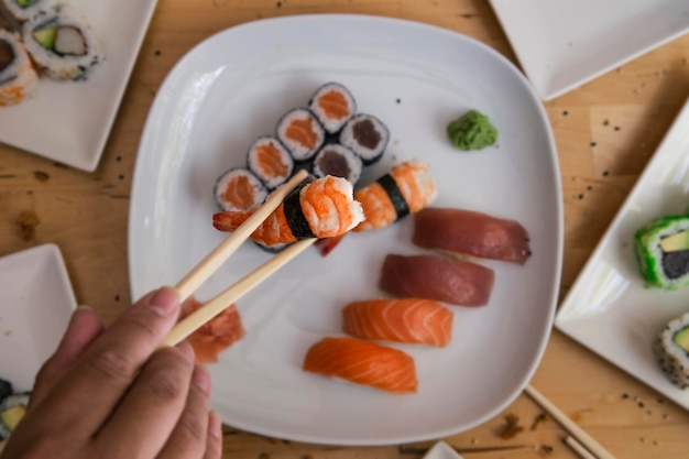 Imagem recortada de homem segurando sushi com pauzinhos em foco seletivo de placa