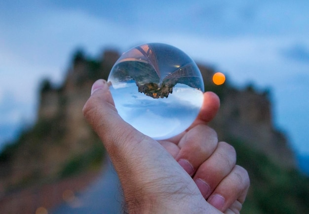 Imagem recortada de mão de homem segurando bola de cristal contra a montanha