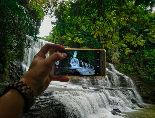 Foto imagem recortada de mão fotografando cachoeira através de telefone celular