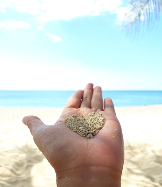 Foto imagem recortada de mão segurando forma de coração de areia na praia