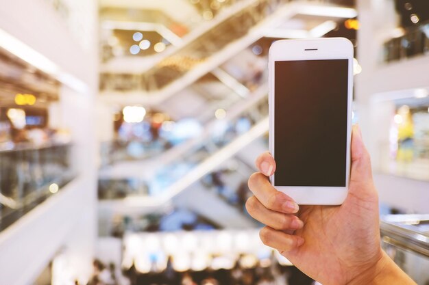 Foto imagem recortada de mão segurando smartphone em uma loja de departamentos