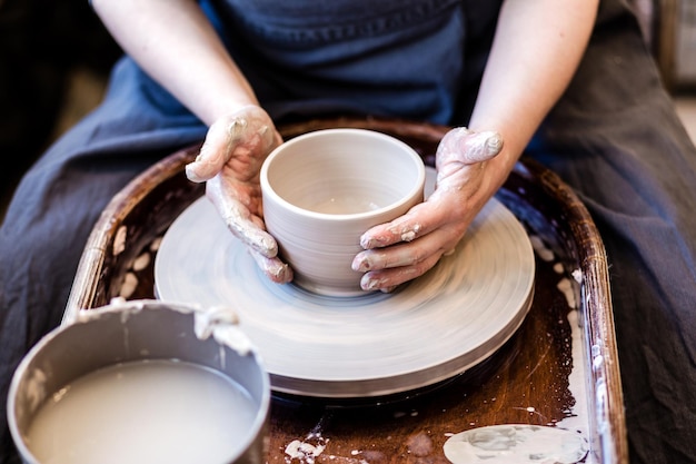 Imagem recortada de mulher de cerâmica irreconhecível trabalhando com roda de cerâmica em oficina aconchegante fazendo vaso ou caneca pessoas criativas