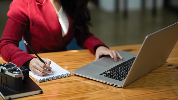 Imagem recortada de mulher de negócios inteligente profissional, trabalhando no computador laptop e fazendo anotações em blocos de notas na mesa dela.