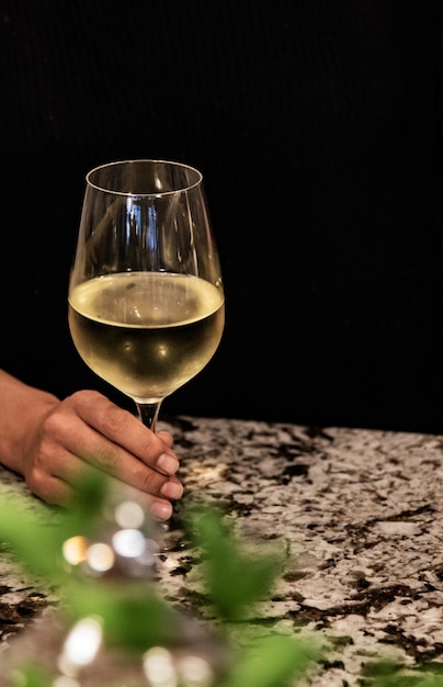 Imagem recortada de mulher segurando um copo de vinho na mesa contra um fundo preto