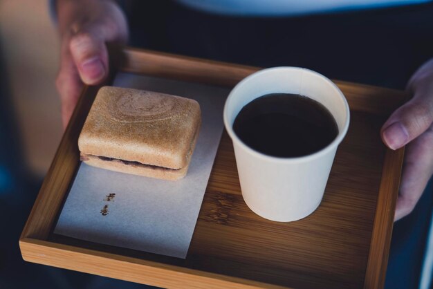 Foto imagem recortada de pessoa segurando xícara de café e biscoito em bandeja