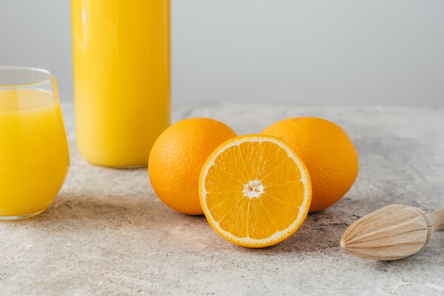 Imagem recortada de suco de laranja em vidro, três laranjas maduras e espremedor de frutas de madeira