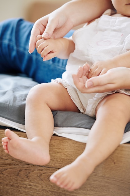 Imagem recortada de um bebê sentado na cama com a mãe