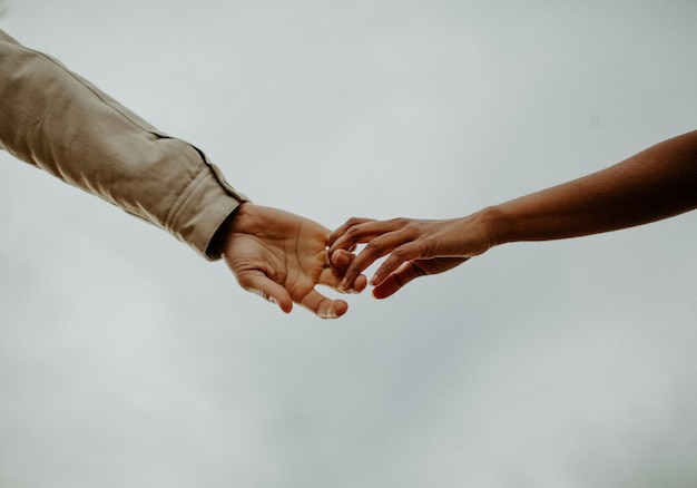 Imagem recortada de um casal de mãos dadas contra um céu claro