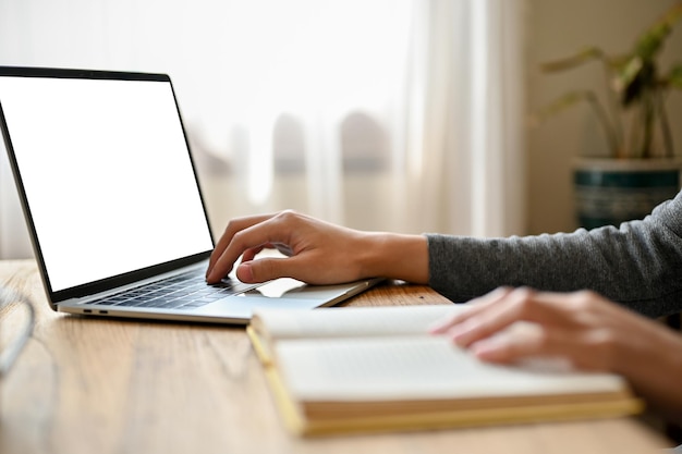 Imagem recortada de um estudante universitário do sexo masculino usando seu laptop enquanto pesquisa informações em um livro