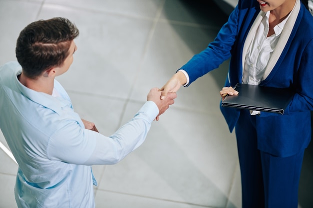 Imagem recortada de um gerente de vendas sorridente, apertando a mão do cliente ao cumprimentá-lo na concessionária de automóveis