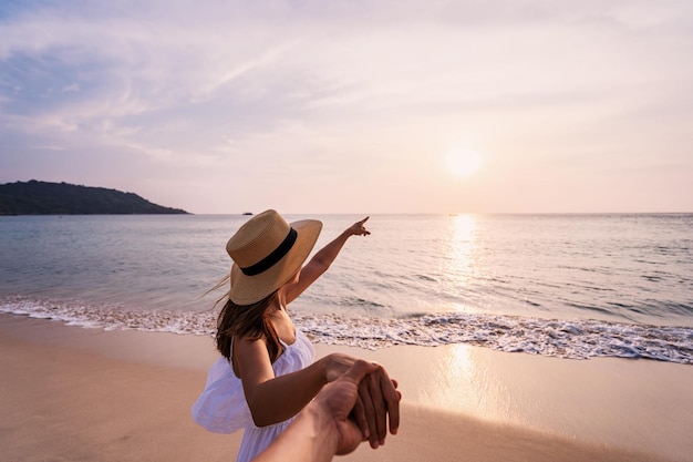 Imagem recortada de um homem segurando a mão de uma mulher na praia contra o céu durante o pôr do sol