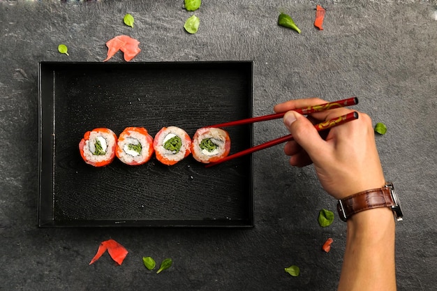 Imagem recortada de um homem segurando sushi com pauzinhos em um prato