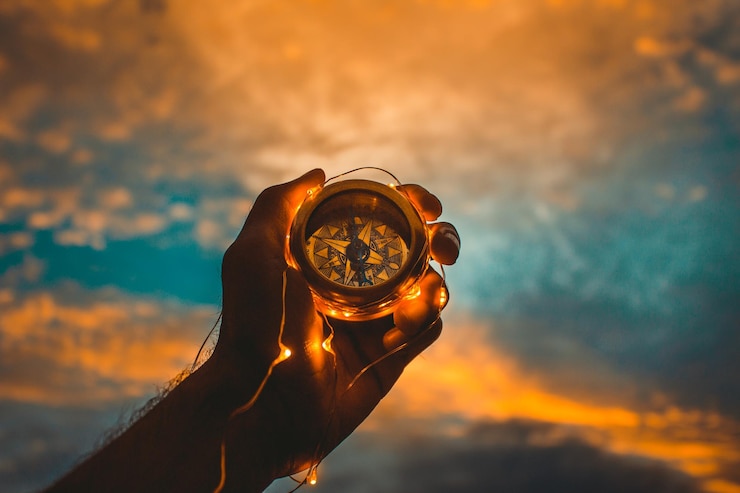 Foto imagem recortada de um homem segurando uma luz de corda iluminada e uma bússola de navegação contra um céu nublado durante o pôr do sol
