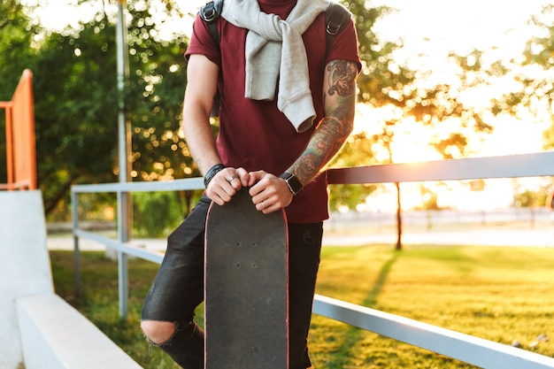 Imagem recortada de um jovem parado na rampa da pista de skate com um skate