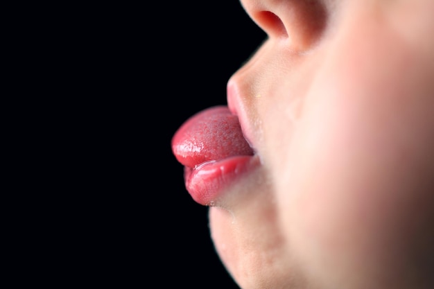 Imagem recortada de uma criança estendendo a língua contra um fundo preto