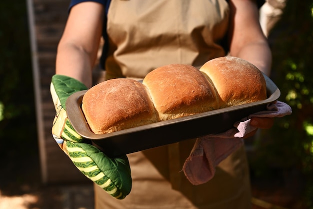 Imagem recortada de uma dona de casa segurando um recipiente de cozimento com pão integral caseiro crocante recém-assado quente