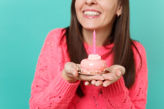 Imagem recortada de uma jovem sorridente numa camisola de malha rosa segurando nas mãos um bolo com vela isolada no retrato de estúdio de fundo de parede azul turquesa. Conceito de estilo de vida de pessoas. Simule o espaço da cópia.