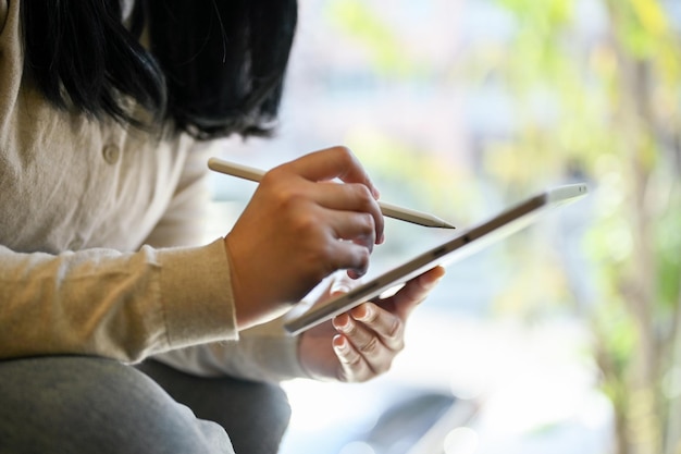Imagem recortada de uma mulher asiática segurando caneta stylus usando tablet digital trabalhando em seu projeto
