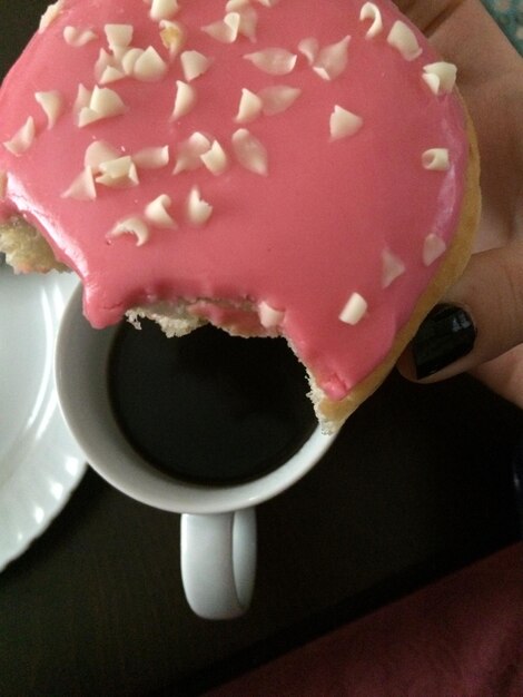 Imagem recortada de uma mulher com a mão segurando um donut com uma xícara de café