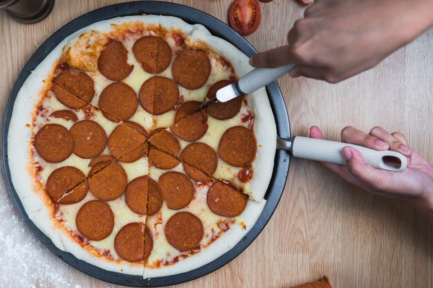 Foto imagem recortada de uma pessoa cortando pizza na mesa