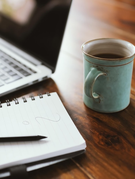 Imagem recortada de xícara de café fresco por diário e laptop na mesa