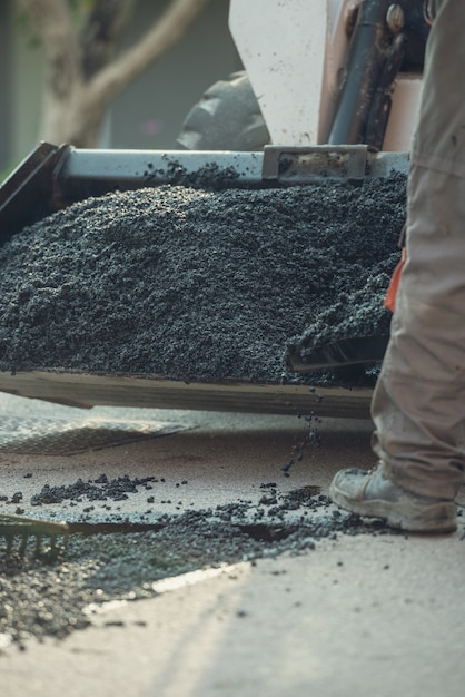 Imagem retro de um trabalhador pegando mistura de asfalto com uma pá de um carrinho de mão para consertar um inchaço na rua.