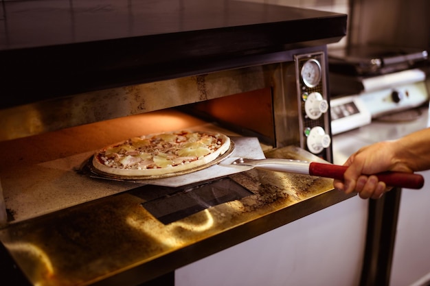 Foto imagem sem rosto de cozinheiro colocando pizza em pedra no forno em um café