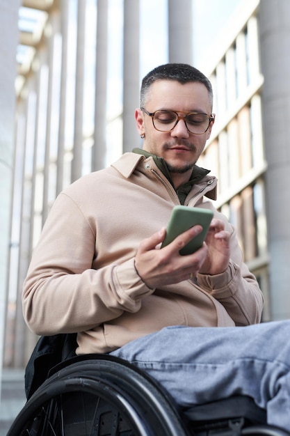 Imagem vertical de jovem com deficiência digitando mensagem em seu smartphone enquanto caminhava ao ar livre