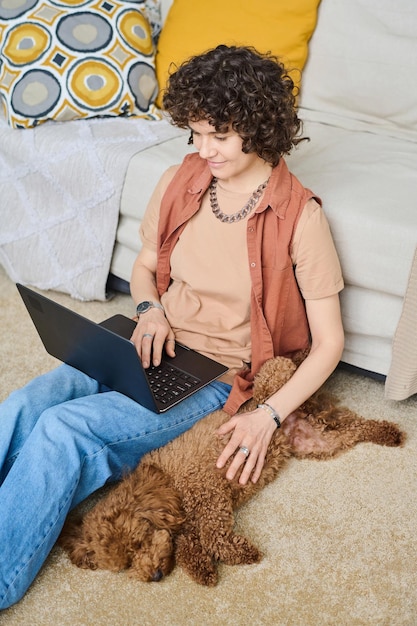 Imagem vertical de jovem descansando em casa com cachorro e usando laptop