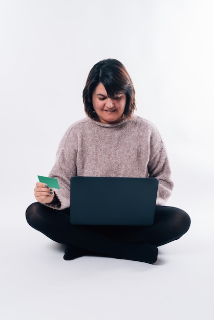 Imagem vertical de mulher sentada fazendo compras online. Mulher sentada com um laptop e um cartão de crédito em fundo branco