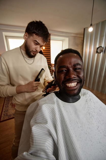 Foto imagem vertical de um homem afro-americano fazendo um retrato selfie enquanto corta o cabelo em uma barbearia