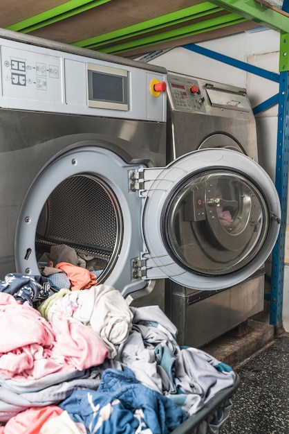 Imagem vertical de uma pilha de roupa na frente de uma máquina de lavar em uma lavanderia