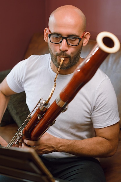 Imagem vertical jovem músico latino tocando fagote em casa lendo partituras