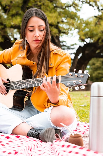 imagem vertical jovem tocando violão, praticando músicas no parque.