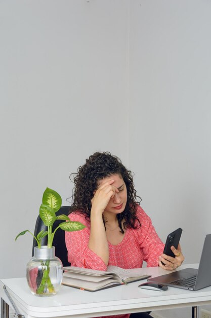 Imagem vertical mulher preocupada trabalhando com seu laptop e telefone celular em seu escritório em casa