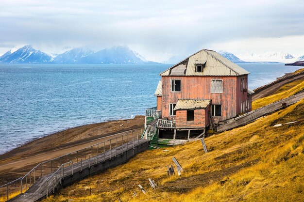 Imagen 4K de una casa abandonada en el asentamiento de Barentsburg Montañas cubiertas de nieve y nubes en el arco