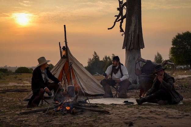 Imagen de acción estilo vintage del grupo de vaqueros Siéntese y relájese y tome un café por la mañana acampando a la luz dorada del sol de la mañana