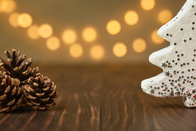 Imagen de adorno de pino de Navidad blanca en un lado y conos de pino en el otro lado en la mesa de madera marrón con luces de Navidad de fondo desenfocado