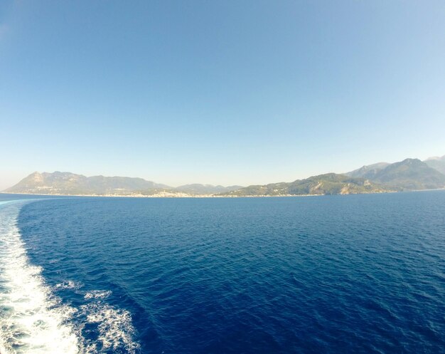 Imagen del agua de un barco en movimiento en el fondo una isla montañosa y agua azul oscuro