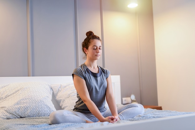 Imagen de ajuste hermosa mujer de mediana edad sentada en su cama en posición de loto.