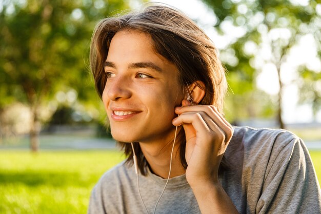 Imagen de alegre joven escuchando música con auriculares en el parque.