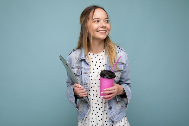 Imagen de la alegre mujer rubia europea sonriendo y de pie contra la pared azul aislada con plata