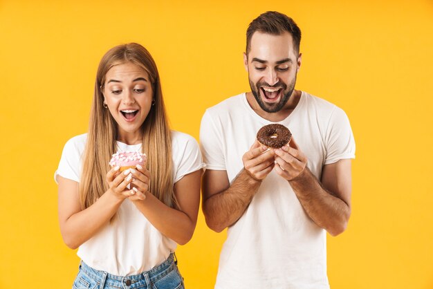 Imagen de la alegre pareja hombre y mujer sonriendo mientras sostiene dulces donas juntos aislado sobre pared amarilla